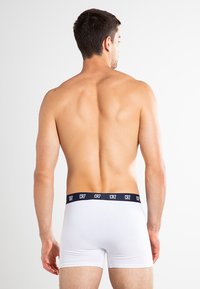 White boxer shorts with a navy CR7 elastic waistband, fitted design, and cotton material, viewed from the back. Skin is visible above the shorts.
