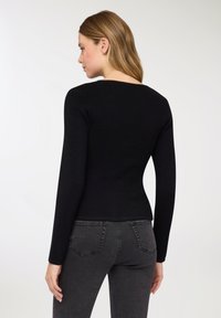 Maglione nero a coste con maniche lunghe, design aderente e scollo dritto, abbinato a jeans in denim grigio, visto da dietro.