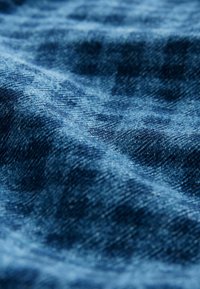 Gros plan sur un tissu en denim bleu montrant la texture et le motif de tissage avec des plis doux et des variations d'éclairage.