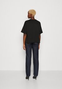 T-shirt nera oversize a maniche corte, abbinata a jeans dritti blu scuro e scarpe con tacco nere, vista da dietro.