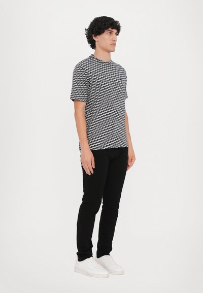 Short-sleeve shirt in black and white wave pattern, paired with slim black pants and white sneakers. Minimalist design, relaxed fit.