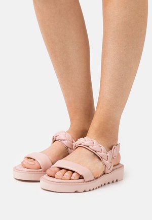 Helle rosa Sandalen mit dicker Sohle, ausgestattet mit geflochtenen Riemen und einem verstellbaren Knöchelriemen. Das Material hat eine glatte, matte Textur.