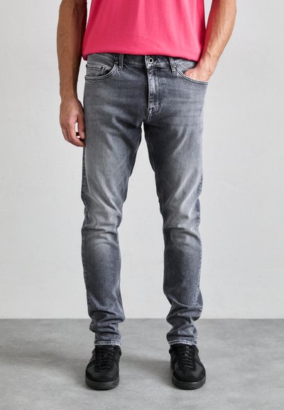 Jeans en denim gris avec une coupe fuselée, présentant un léger délavage. Fini avec cinq poches et une fermeture éclair. Associés à des baskets noires.