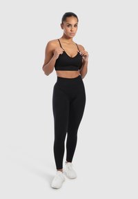 Zwarte sportbeha met dunne banden en een V-hals ontwerp, gecombineerd met hoge zwarte leggings; naadloze textuur, strakke pasvorm.