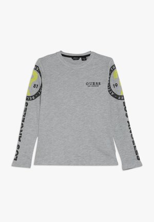 Grå langærmet skjorte med "GUESS Los Angeles" tekst på brystet og grafiske cirkulære logoer med tekst på begge ærmer.