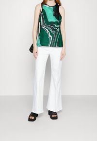 Top sin mangas con estampado verde y negro y escote redondo, combinado con pantalones acampanados blancos y sandalias negras con plataforma.