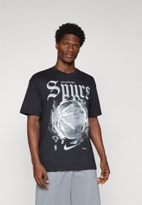 Czarny t-shirt z dużą grafiką San Antonio Spurs, motywem koszykarskim i logo Nike. Krótkie rękawy i luźny krój.
