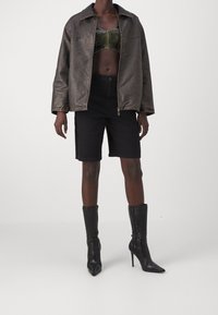 Metalická bronzová oversized bunda, tmavý crop top, černé džíny šortky a vysoké černé stiletto boty s texturovaným designem.