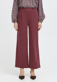 Pantaloni largi dintr-un material burgundy închis, cu pliuri frontale, talie înaltă și o textură netedă. Asortați cu tocuri întunecate, rotunde.