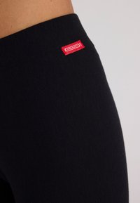 Zwarte legging gemaakt van een zachte, rekbare stof met een gladde textuur; heeft een klein rood label nabij de tailleband.