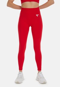Leggings rouges taille haute en tissu extensible, avec un petit logo blanc sur la cuisse gauche et une texture lisse et élégante.