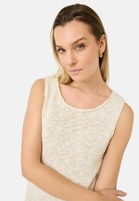 Ljust beige ärmlös stickad topp med rund halsringning och texturerad yta. Har råa kanter och en lös passform.