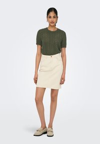 Knit olive green short-sleeve top with a textured pattern; cream denim mini skirt; beige loafers with a bow detail.