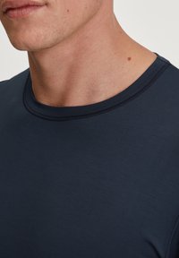 Marineblauwe crew neck t-shirt van zacht, rekbaar materiaal. Heeft een gladde textuur met subtiele stiksels langs de halslijn.