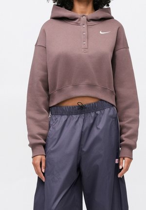 Personne portant un sweat à capuche court mauve Nike avec des boutons et un pantalon de sport ample gris foncé avec une taille à cordon.