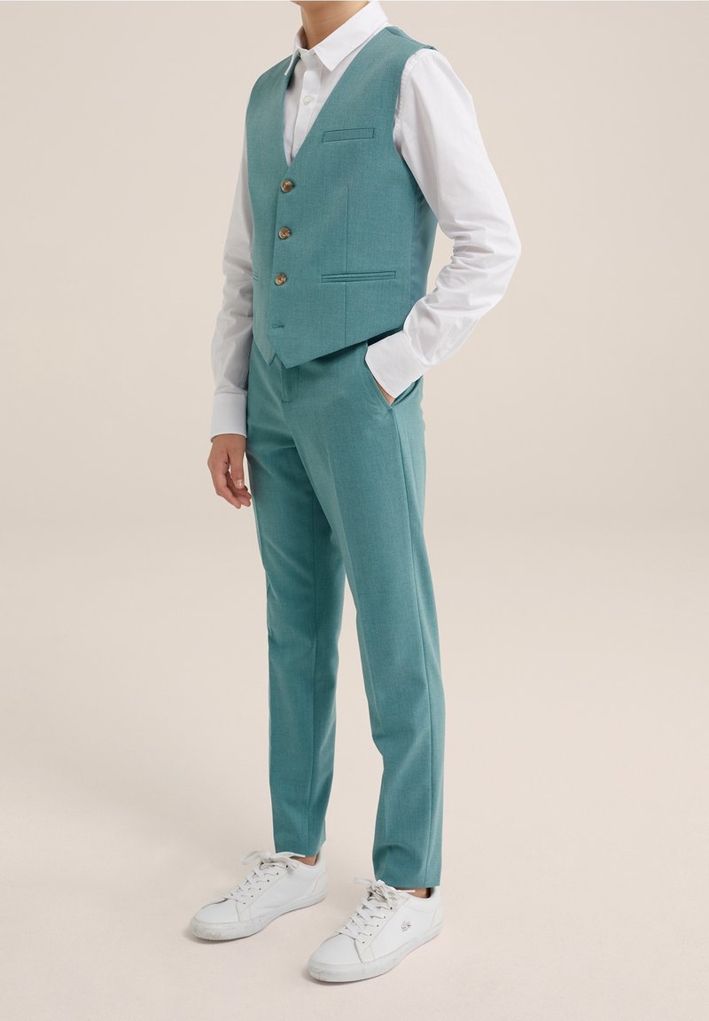Tyrkysová vesta se třemi knoflíky, přední kapsou, v kombinaci s ladícími kalhotami a bílými teniskami. Hladká látka, přiléhavý střih.