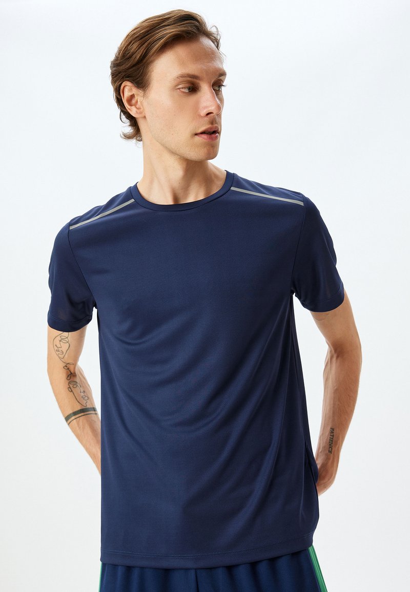 Marinblå atletisk t-shirt, kort ärm, rund halsringning, slät yta, med reflexdetaljer på axelsömmarna.