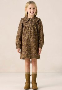 Robe à imprimé léopard marron avec un grand col, des manches longues et une fermeture à boutons. Associée à des bottines marron et des chaussettes en maille.
