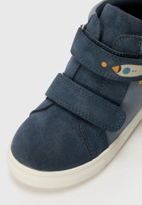 Mörkblå mockahögsko med två kardborreband. Har en raketdesign på sidan och en vit gummisul.