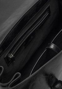 Intérieur de sac à main en cuir noir avec une poche zippée, doublure en tissu et texture lisse. Comprend une bandoulière pour le transport.