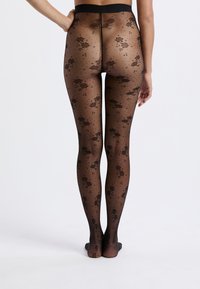 Collant neri trasparenti con motivo in pizzo floreale, texture liscia e una ampia vita nera, progettati per un look aderente.