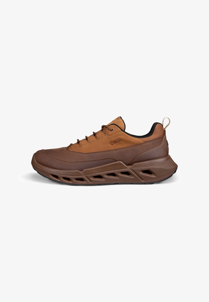 Chaussure de sport marron avec une tige texturée, des accents en mesh, une semelle épaisse avec un design découpé et une languette au talon.