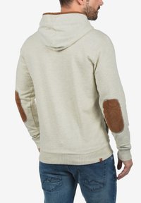 Lichtgrijze sweatshirt met capuchon en een gestructureerde afwerking, voorzien van bruine suède elleboogpatches en een geribbelde zoom. Ontworpen met een casual pasvorm.