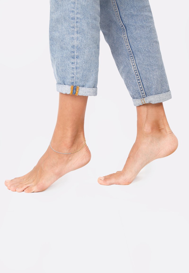 Lysblå denim bukser rullet op ved manchetten, parret med bare fødder. Et delikat anklet i guld og sølv pryder anklen og fremhæver hudtonen.