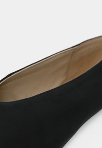 Zwarte ballerina met beige binnenvoering, een gladde textuur en een ronde neus, tegen een effen lichte achtergrond.