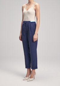 Pantaloni in lino blu navy con vita regolabile, orli con risvolto, abbinati a una canotta beige a coste con spalline sottili e scollatura a V.