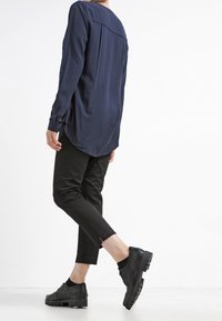 Marineblå langærmet skjorte med rund kant, parret med sorte tapered bukser og teksturerede sorte sneakers med lav profil og gummisål.