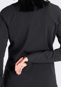 Top negro de manga larga con un diseño ajustado, textura suave y agujeros para los pulgares en las mangas, que muestra una construcción sin costuras en los hombros.