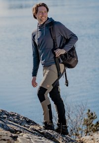Wandeloutfit met een marineblauwe capuchontrui en twee-kleurige broeken (lichtbruin en zwart) met verstevigde kniestukken, gecombineerd met zwarte schoenen.