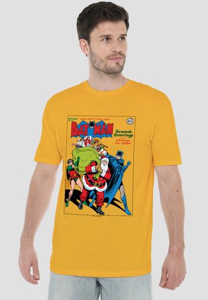 Man wearing yellow T-shirt featuring Batman, Robin, and Santa Claus carrying a large sack of gifts in comic-style design.