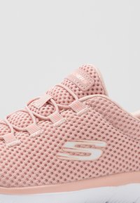 Baskets en maille rose avec un motif texturé, présentant des lacets ton sur ton, une semelle rose clair et un logo de marque blanc sur le côté.