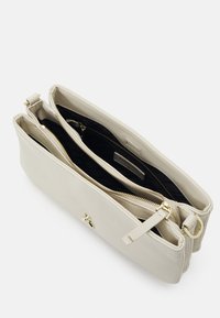 Bolso de cuero crema con compartimentos con doble cremallera, acentos de hardware dorado y un acabado texturizado. Interior forrado en tela negra.