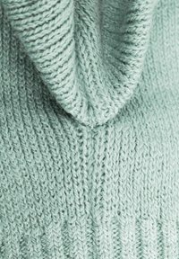 Light green knitted sweater with a textured ribbed pattern and a folded collar. Soft wool fabric visible with prominent stitching details.