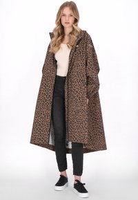 Barna leopárdmintás hosszú kabát kapucnival, laza fazonú és oldalzsebbel, fekete skinny farmerrel és fekete tornacipővel párosítva.