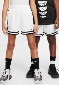 Δύο άτομα φορούν λευκά σορτς μπάσκετ με μαύρες ρίγες, μαύρες κάλτσες Nike και αθλητικά παπούτσια ασπρόμαυρα, στέκονται δίπλα το ένα στο άλλο.