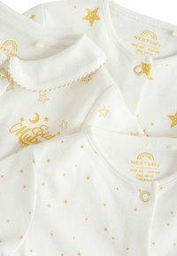 Drei weiße Babykleidungsstücke mit goldenen Sternmustern, einem Kragen mit dekorativem Besatz und einem bedruckten Mond- und Textdesign.