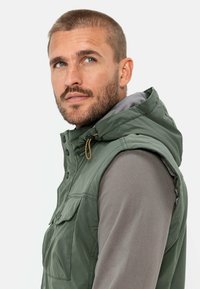 Grüne ärmellose Weste mit Kapuze, zwei Fronttaschen, einem Reißverschluss und einem Kordelzug. Das Innenfutter ist grau.