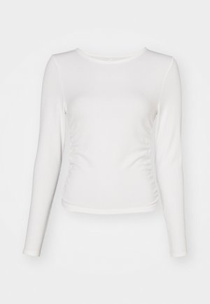 White long-sleeve top made of ribbed fabric, featuring a fitted design with ruching detail at the sides and a round neckline.