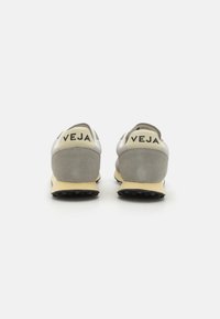 Sneakers cinza de camurça e malha com detalhes amarelos, apresentando uma sola de borracha preta e a marca "VEJA" no calcanhar.
