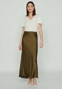 Ελαιοκόκκινη σατέν μακριά φούστα με εφαρμοστή σιλουέτα, συνδυασμένη με λευκό μπλουζάκι κοντού μανικιού και ανοιχτόχρωμα γόβες με μυτερή μύτη.