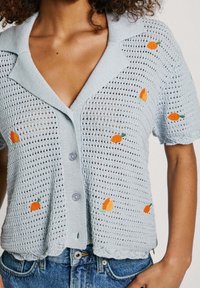 Cardigan corto lavorato a maglia di colore blu chiaro con maniche corte e colletto, caratterizzato da accenti di frutta ricamati arancioni e chiusura con bottoni. Design aperto.