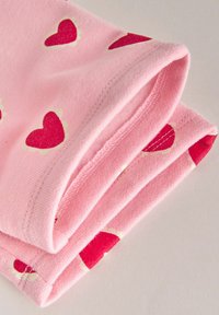 Rosa tyg med små röda hjärtmönster, lätt mjuk textur, prydligt vikt, visar kanter och sömnadsdetaljer.