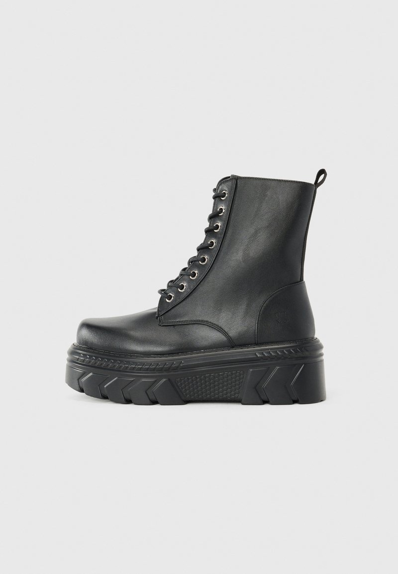 Bota de tornozelo em couro preto com atacadores, sola de plataforma grossa, detalhes texturizados e costura reforçada. Inclui unha alça na parte de trás.