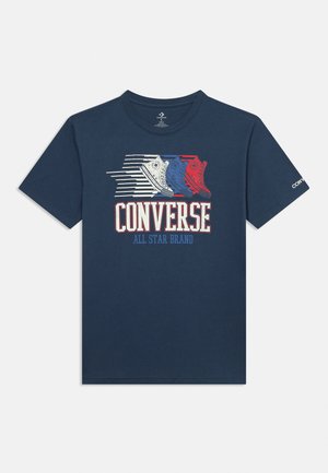Marineblaues T-Shirt mit rotem, weißem und blauem Sneaker-Motiv über den Schriftzügen „CONVERSE“ und „ALL STAR BRAND“ auf der Vorderseite.