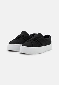 Schwarze Leinensneaker mit einem geknoteten Vorderdesign, weißen Gummisohlen und einer strukturierten Oberfläche, die mit einem gepunkteten Innenfutter ausgestattet ist.