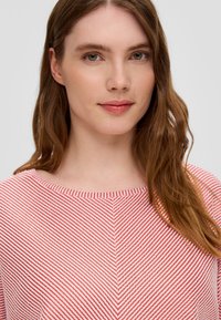 Rood-witte gestreepte top met een brede halslijn en zigzagtextuur. Materiaal lijkt zacht en lichtgewicht, geschikt voor casual wear.